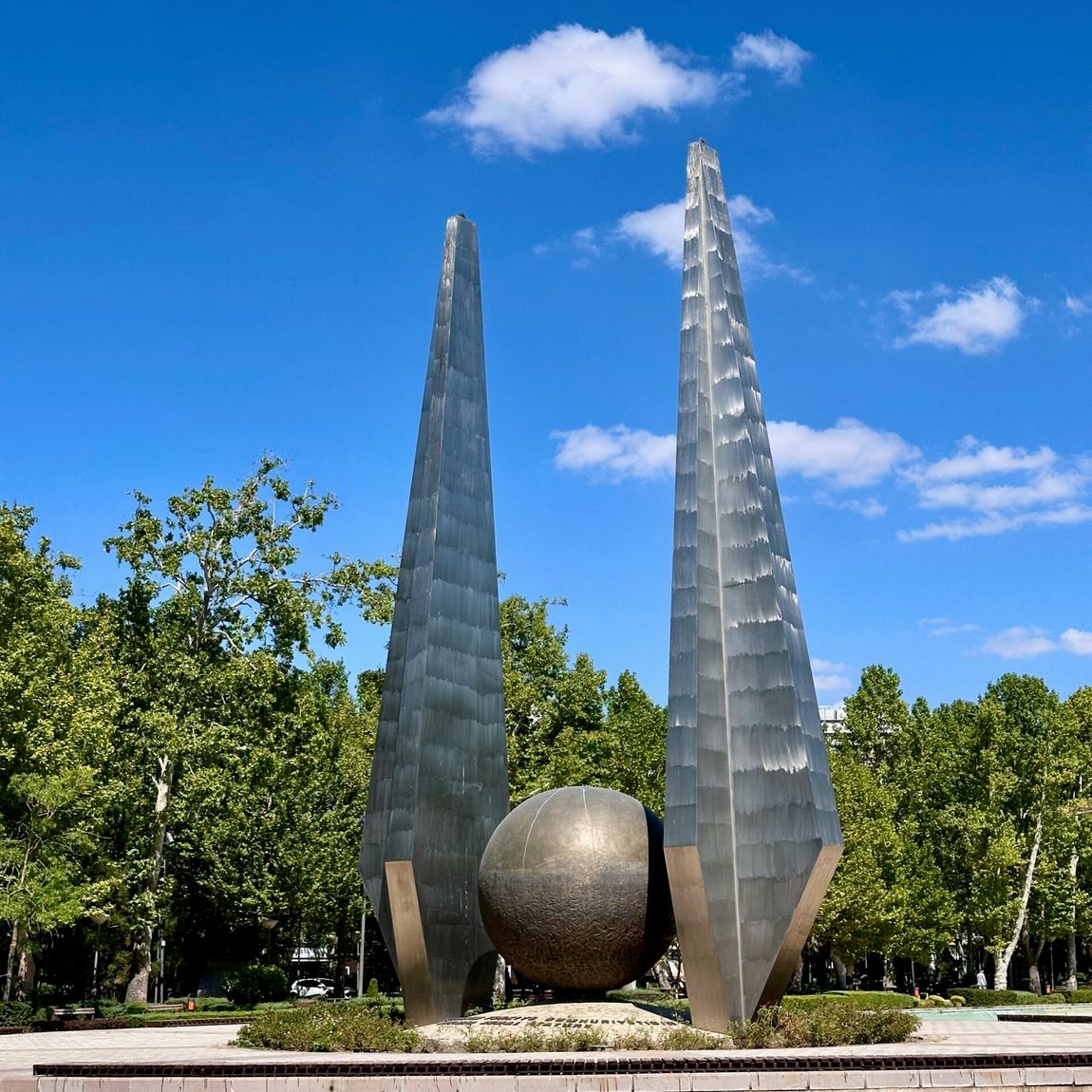 Two tall metallic sculptures and a spherical monument in ankara genclik park, turkey, under a blue sky with clouds