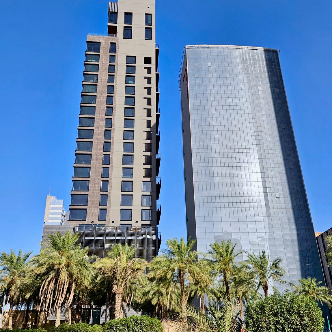 Kuwait city building with a tall apartment tower and a large glass office building, palm trees in front