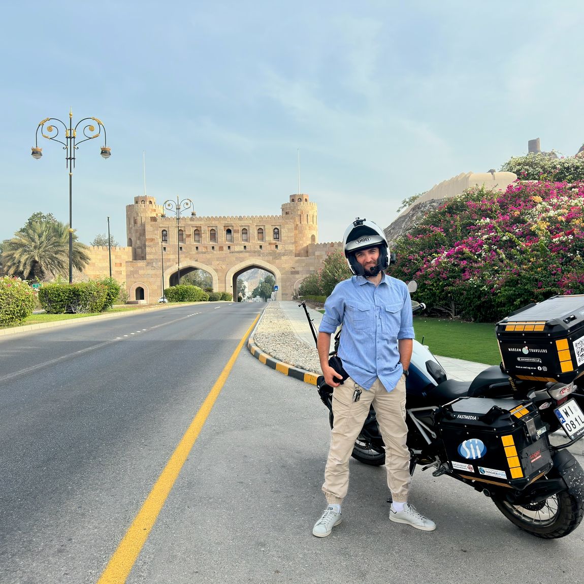 Filip z motocyklem przy muscat gate w omanie, na tle ozdobnej bramy i kwitnących krzewów