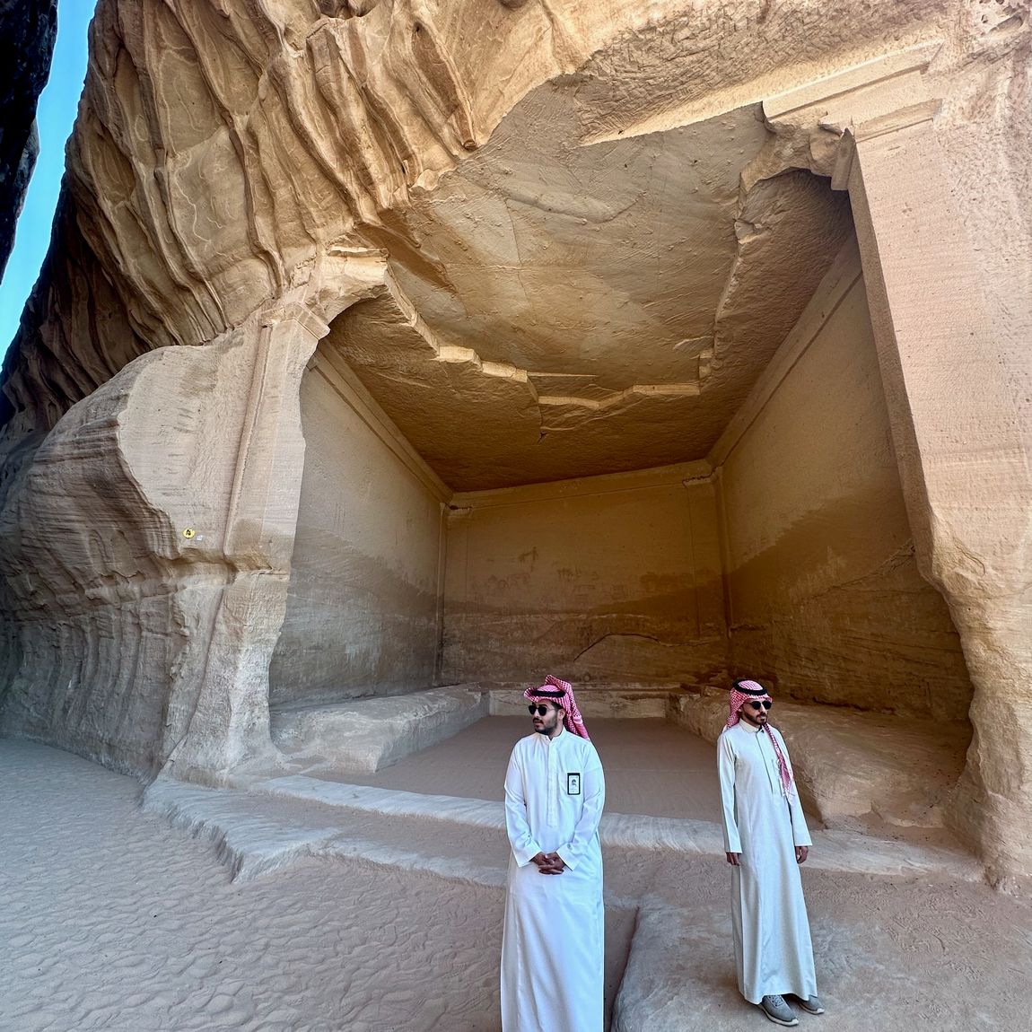 Saudi arabia, al ula al diwan: two men in traditional dress standing in a sandstone cave corridor