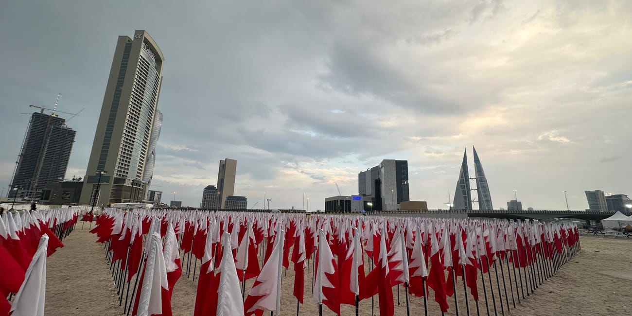Plaża w bahrajnie z setkami flag bahrajnu i panoramą wieżowców o zachodzie słońca.