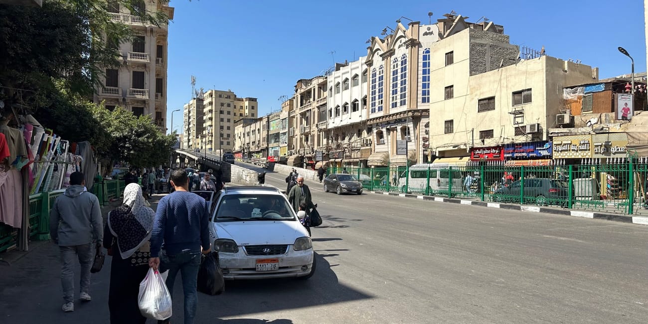 A busy street in egypt with pedestrians, cars, and low-rise buildings under a clear blue sky