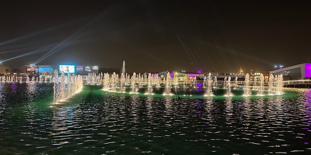 Riyadh boulevard world nocą, z podświetlaną fontanną nad wodą