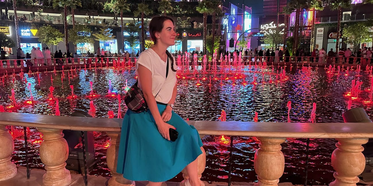 Kobieta siedzi przy fontannie w riyadh boulevard world nocą, na tle kolorowych świateł i tłumu.