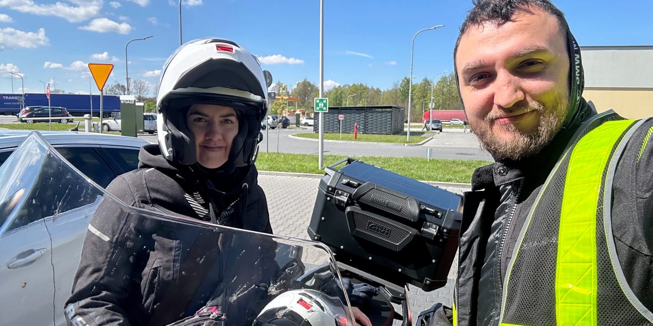 Para motocyklem w wiedniu, dwoje osób w kaskach robi selfie przy motocyklu.