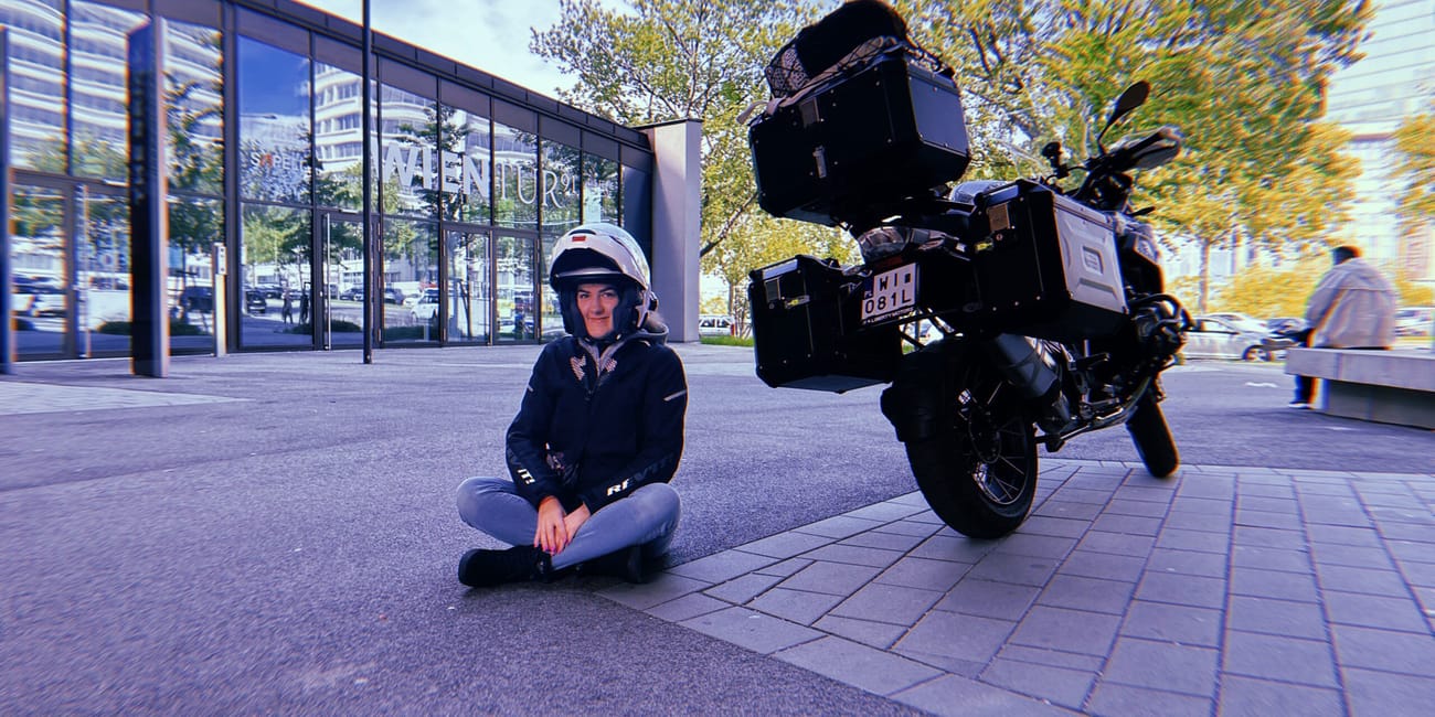 Kobieta w kasku siedzi na ziemi obok motocykla przed wejściem wien.