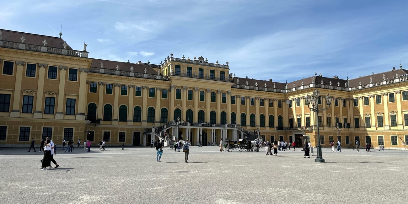 Pałac schönbrunn w wiedniu z dziedzińcem i spacerującymi turystami.