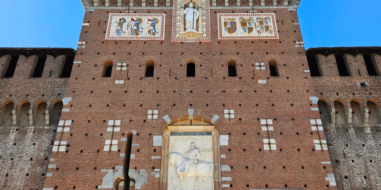 Wieża wejściowa zamku castello sforzesco w mediolanie z zegarem i herbami, z turystami u wejścia.