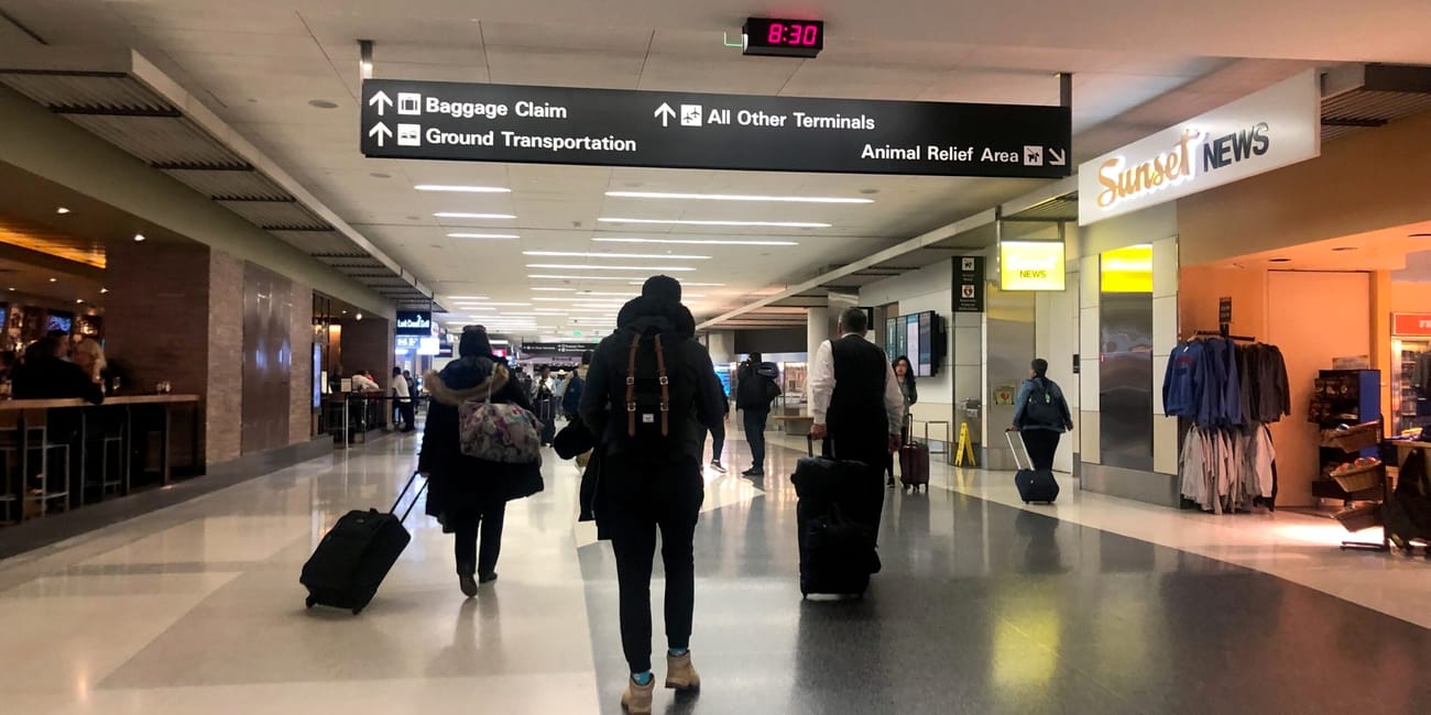 Travelers walking through an airport with signs for baggage claim and lost luggage in the background
