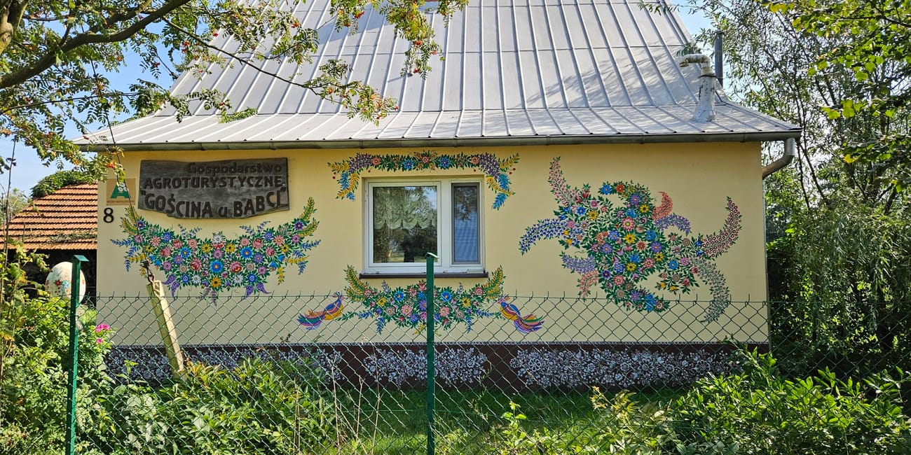 Dom w zalipiu z malowanymi kwiatowymi zdobieniami i napisem o agroturystyce