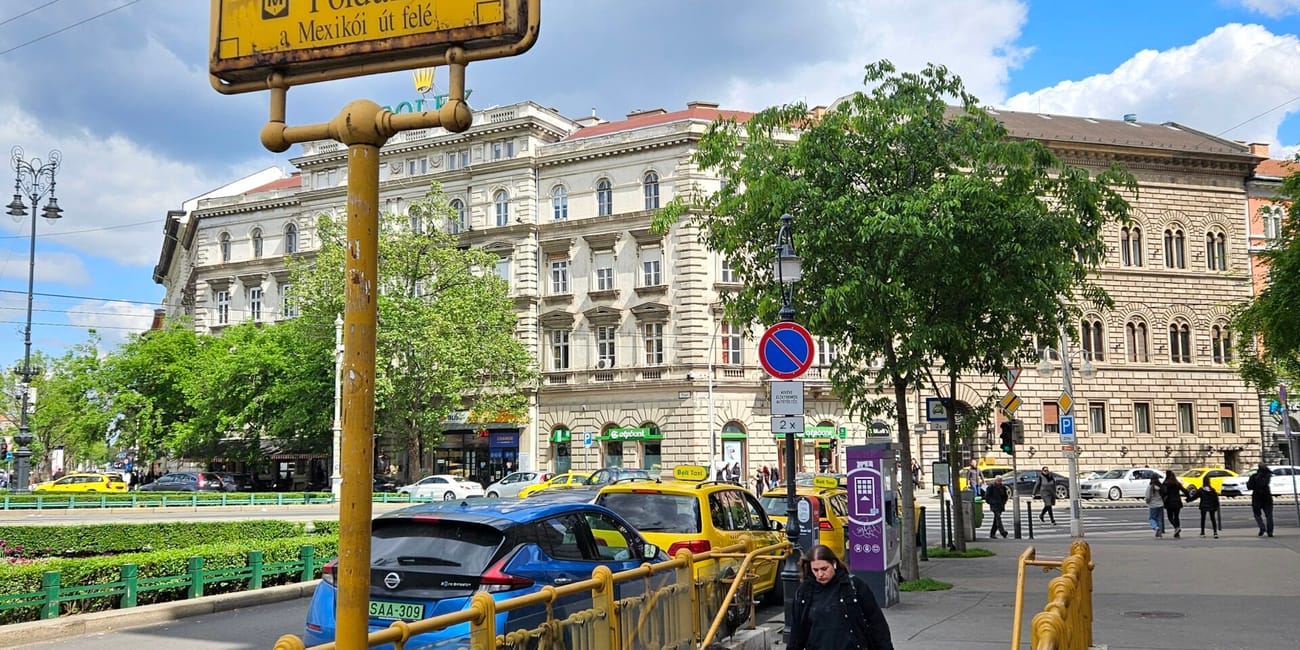 Wejście do stacji metra földalatti przy oktogonie w budapeszcie, z żółtym znakiem i schodami.