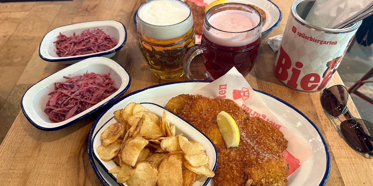 Posiłek w budapeszteńskim biergartenie: panierowany kotlet, frytki, chipsy i piwo w kuflach.