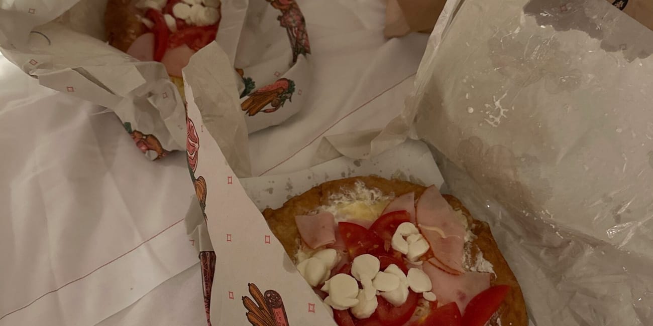 Węgierskie jedzenie na wynos na łóżku w budapeszcie: dwa placki z pomidorami i serem oraz papierowa torba z logo.