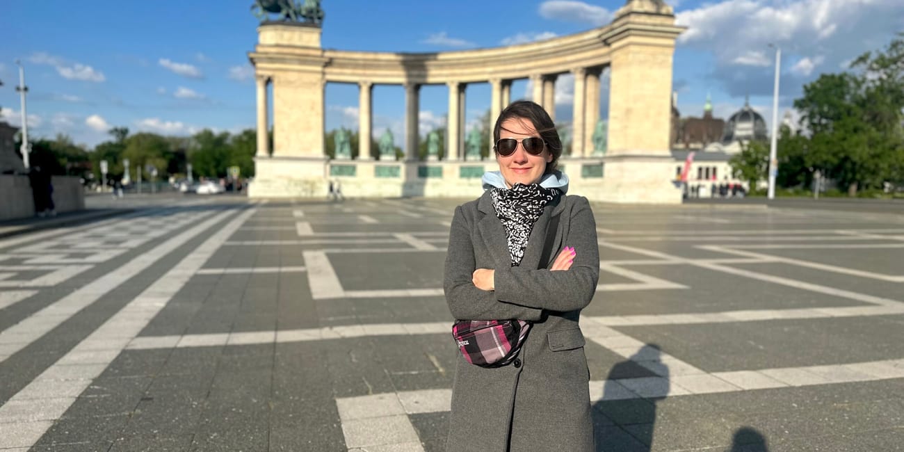 Plac bohaterów w budapeszcie z kobietą na pierwszym planie i pomnikiem w tle.
