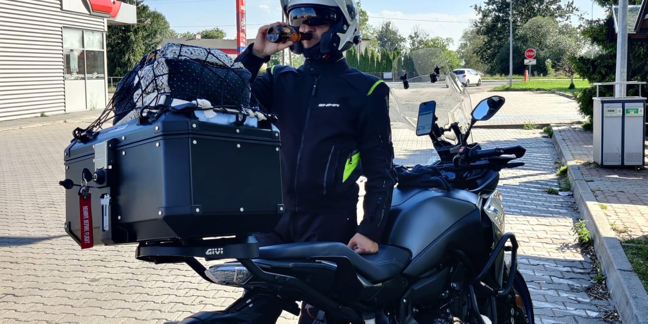 Motocyklista przy czarnym motocyklu w szczecinie, pijący napój na postoju.