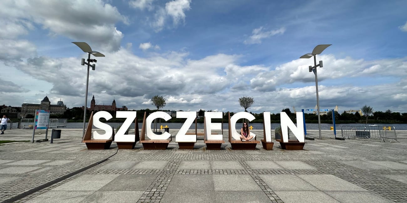 Napis „szczecin” na bulwarze nad wodą, pod zachmurzonym niebem.