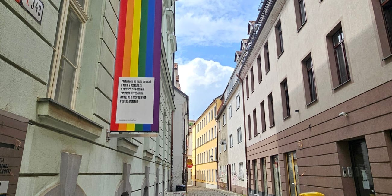 Wąska brukowana uliczka w bratysławie z tęczowym banerem na kamienicy.
