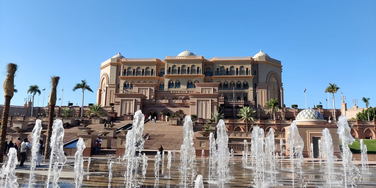 Emirates palace w abu dhabi z fontannami na pierwszym planie i błękitnym niebem.