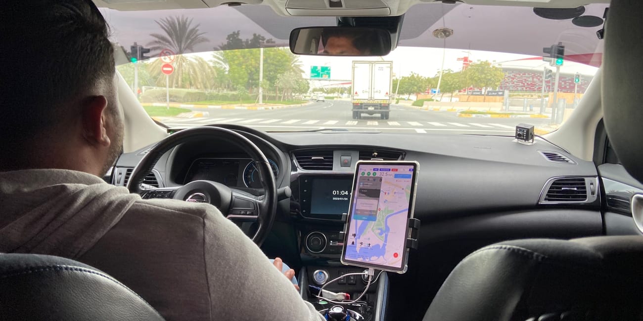 Wnętrze autonomicznego auta txai w abu dhabi, widok z tylnego siedzenia na kierowcę i ekran nawigacji.