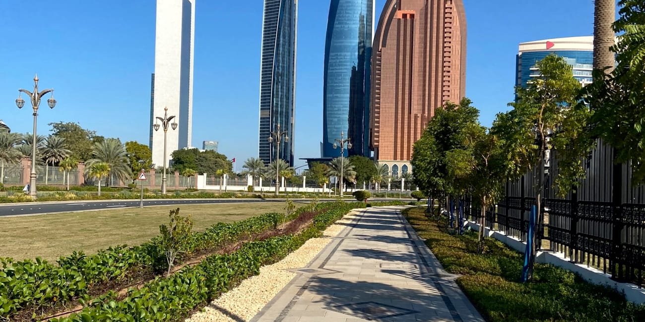 Wieżowce w abu dhabi widziane z zadbanego chodnika wzdłuż zieleni.