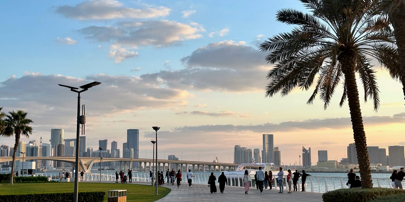 Louvre abu dhabi o zachodzie słońca, z promenadą, palmami i panoramą abu zabi.