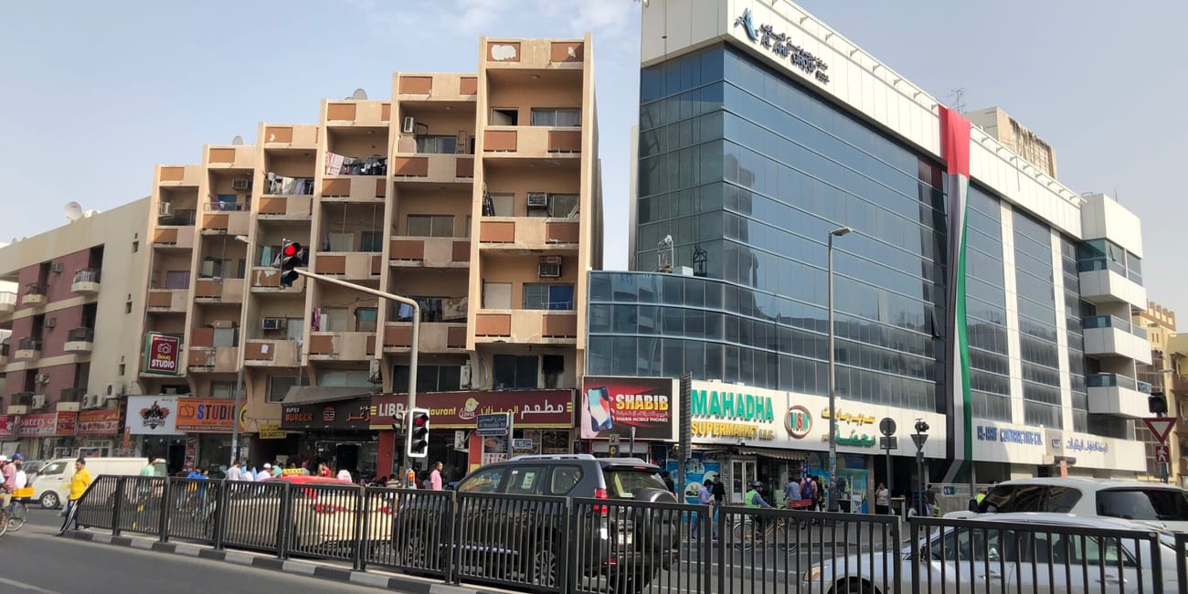 Uliczny widok w dubaju z blokami, nowoczesnym budynkiem i ruchem samochodowym.