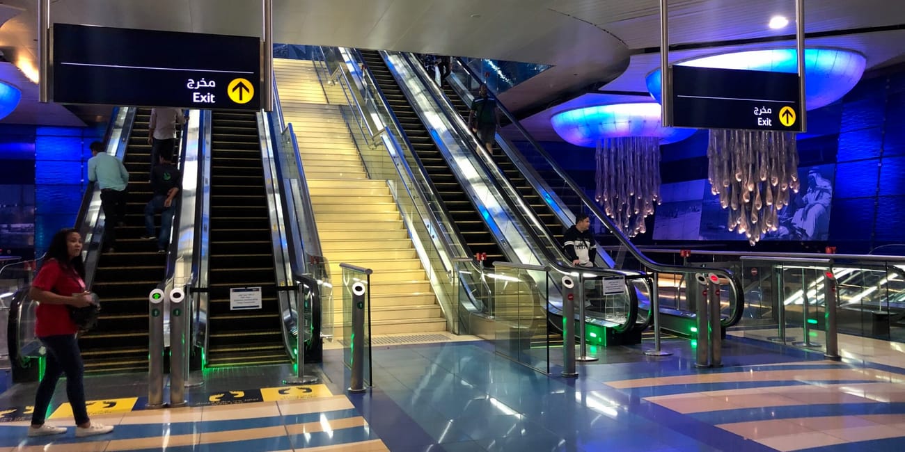 Wnętrze stacji dubai metro z ruchomymi schodami, neonowym oświetleniem i oznaczeniami wyjścia.