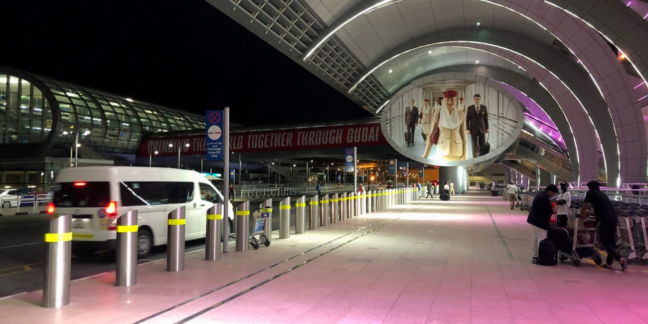 Wejście do dubai airport w dubaju nocą, z podświetlonym zadaszeniem i pasażerami z wózkami bagażowymi
