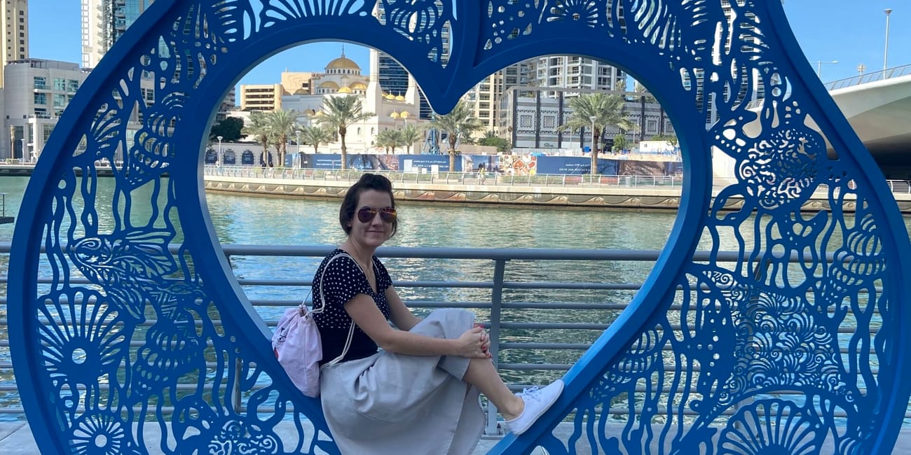 Osoba siedzi w niebieskiej ramie z napisem dubai marina nad wodą i wieżowcami w tle.