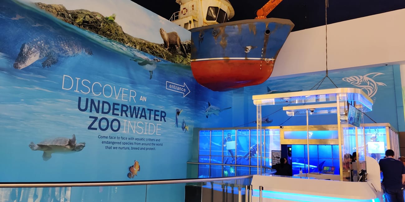 Wejście do dubai aquarium z dużą ekspozycją podwodnego zoo i zawieszonym statkiem.