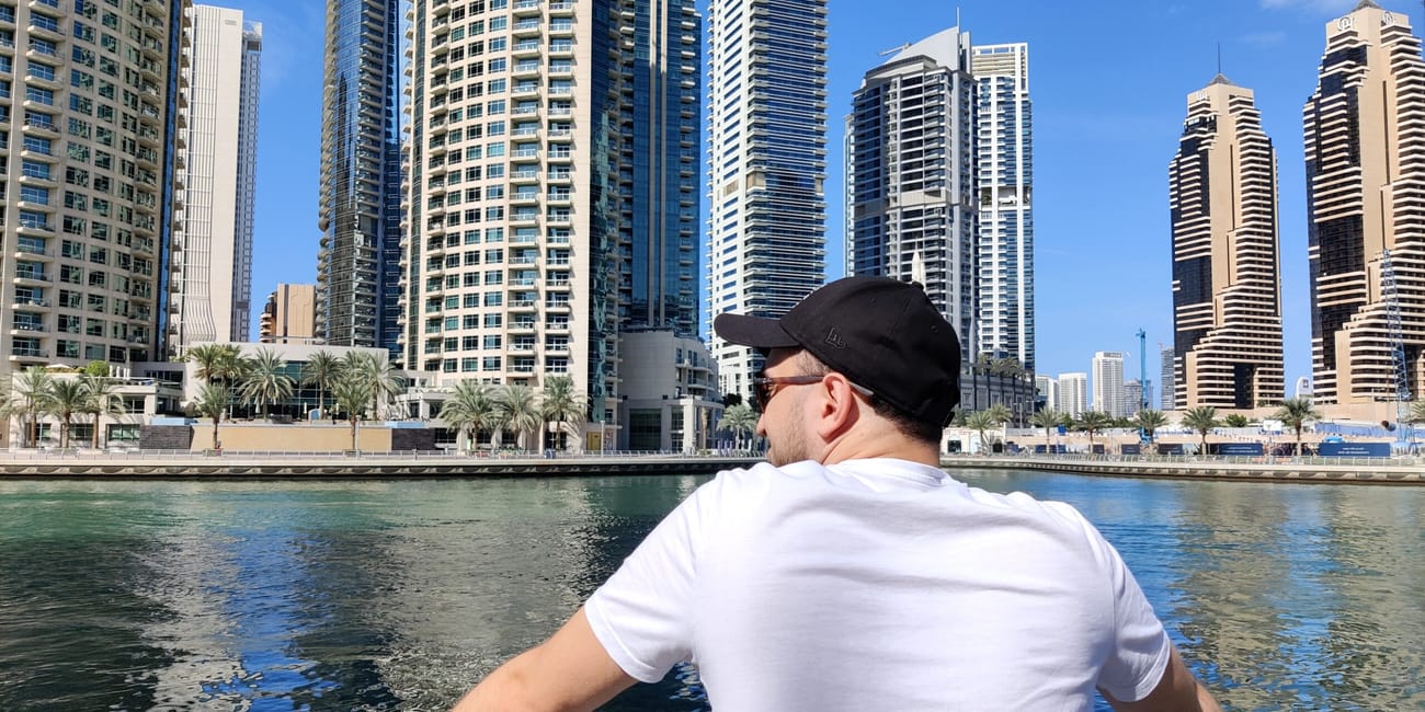Dubai marina z wieżowcami nad wodą, z mężczyzną opartym o barierkę na pierwszym planie