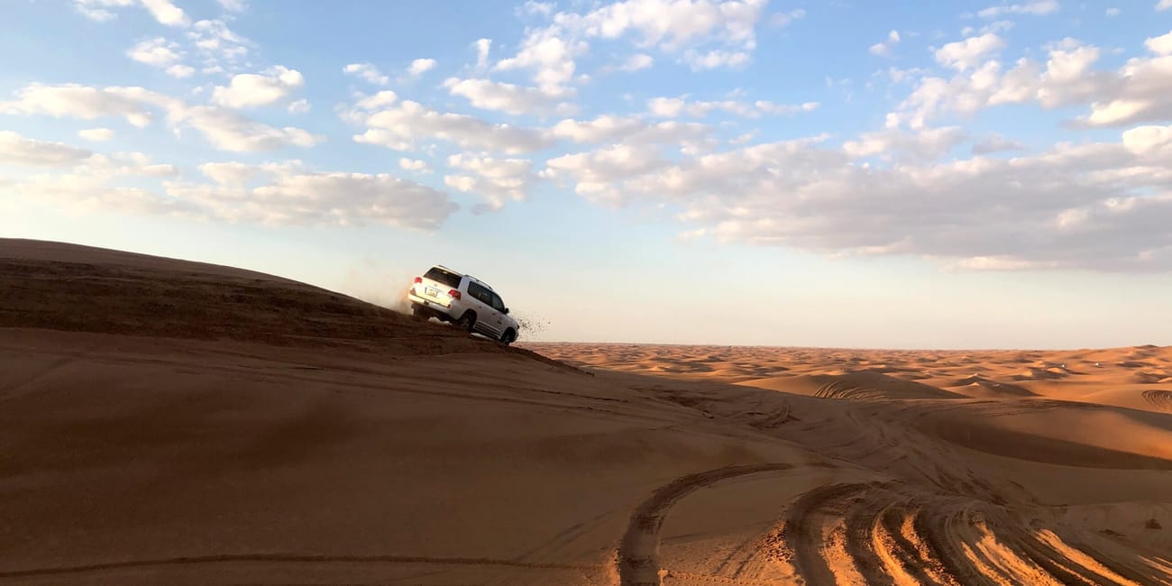 Pojazd terenowy na wydmie w dubai safari, wśród pustynnych wydm pod błękitnym niebem