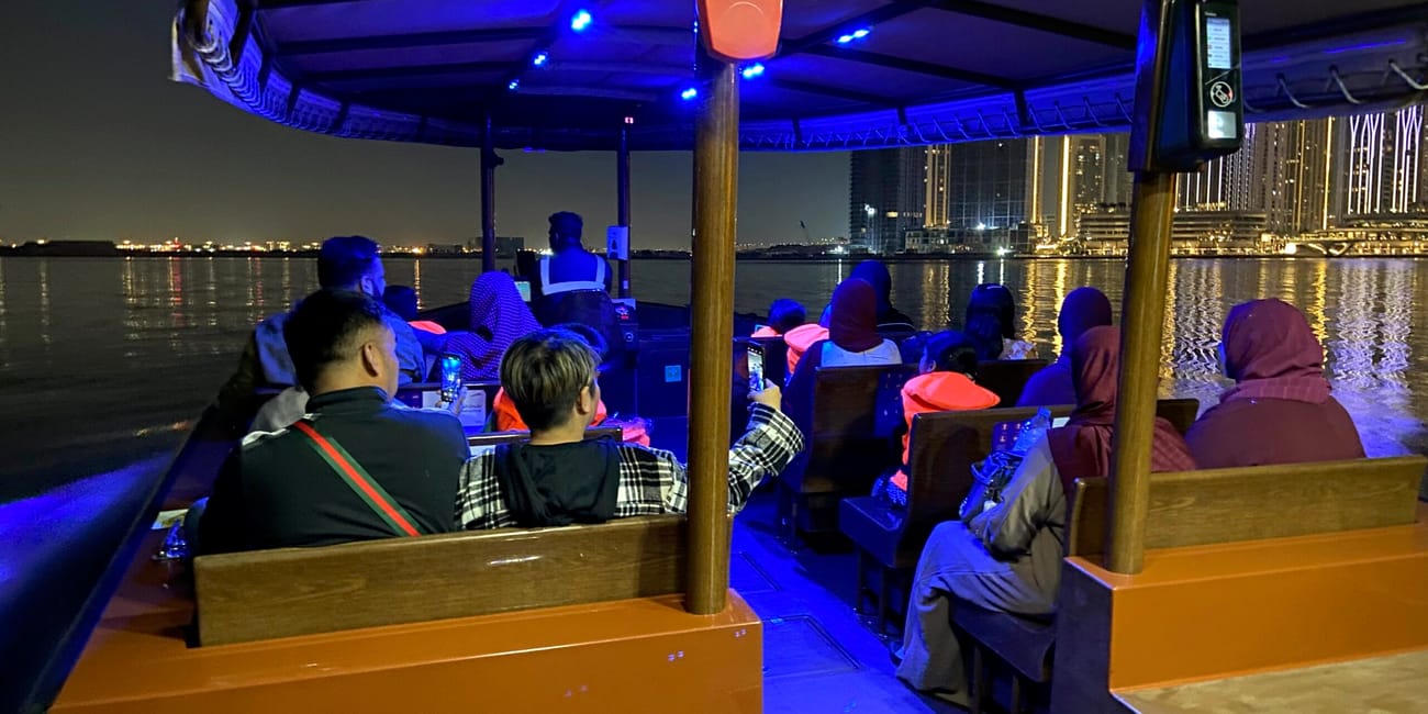 Wieczorny rejs po dubai creek w dubaju z pasażerami na pokładzie i oświetlonymi wieżowcami w tle