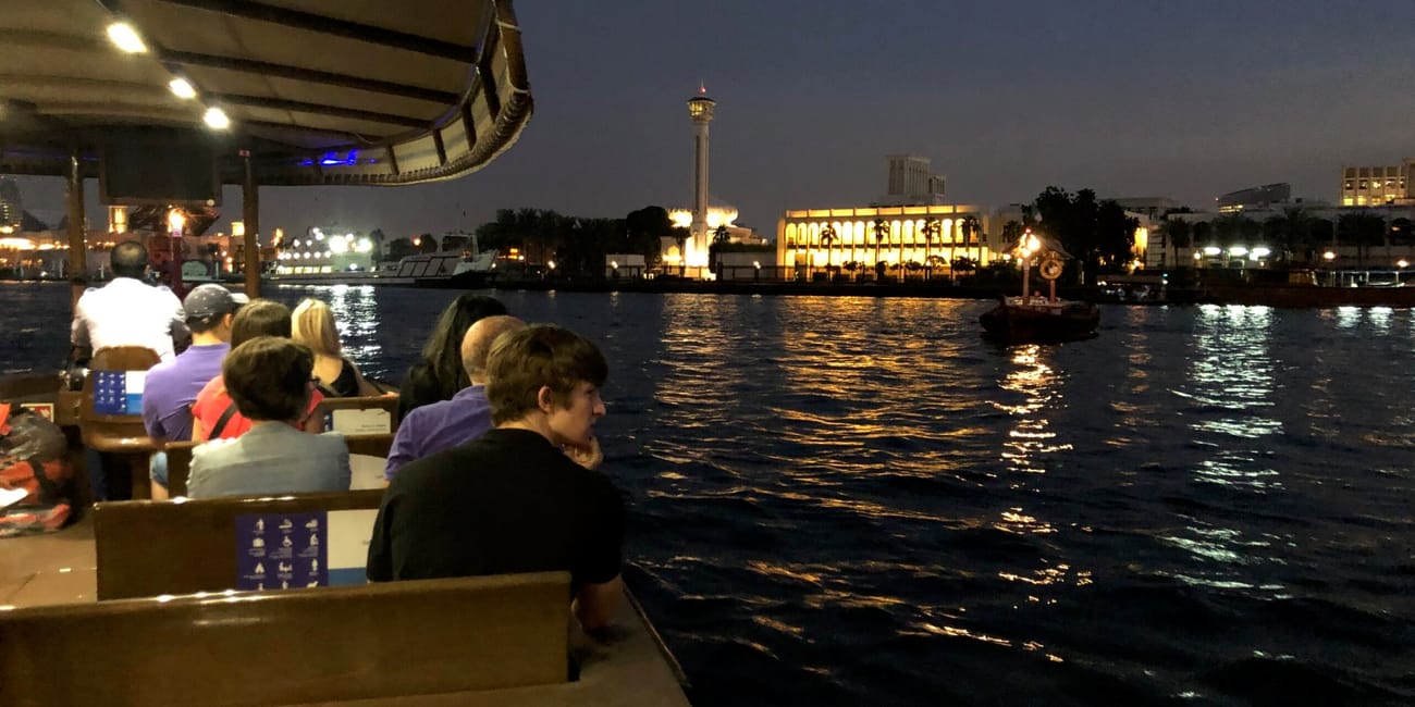 Rejs po dubai creek nocą, z pasażerami na pokładzie i oświetlonym brzegiem w tle