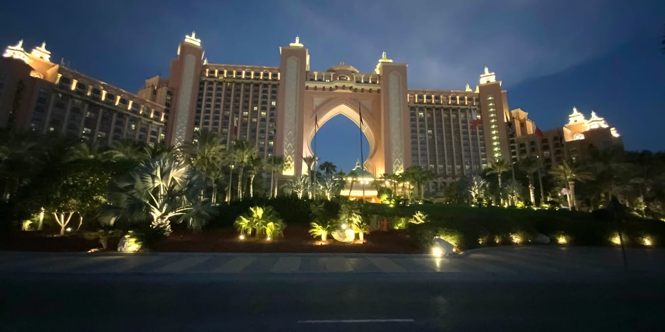 Atlantis hotel w dubaju nocą, podświetlony fasadą i palmami na pierwszym planie
