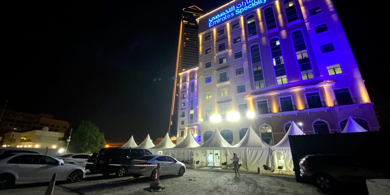 Emirates specialty hospital w dubaju nocą, oświetlony na fioletowo, z parkingiem i namiotami przed budynkiem