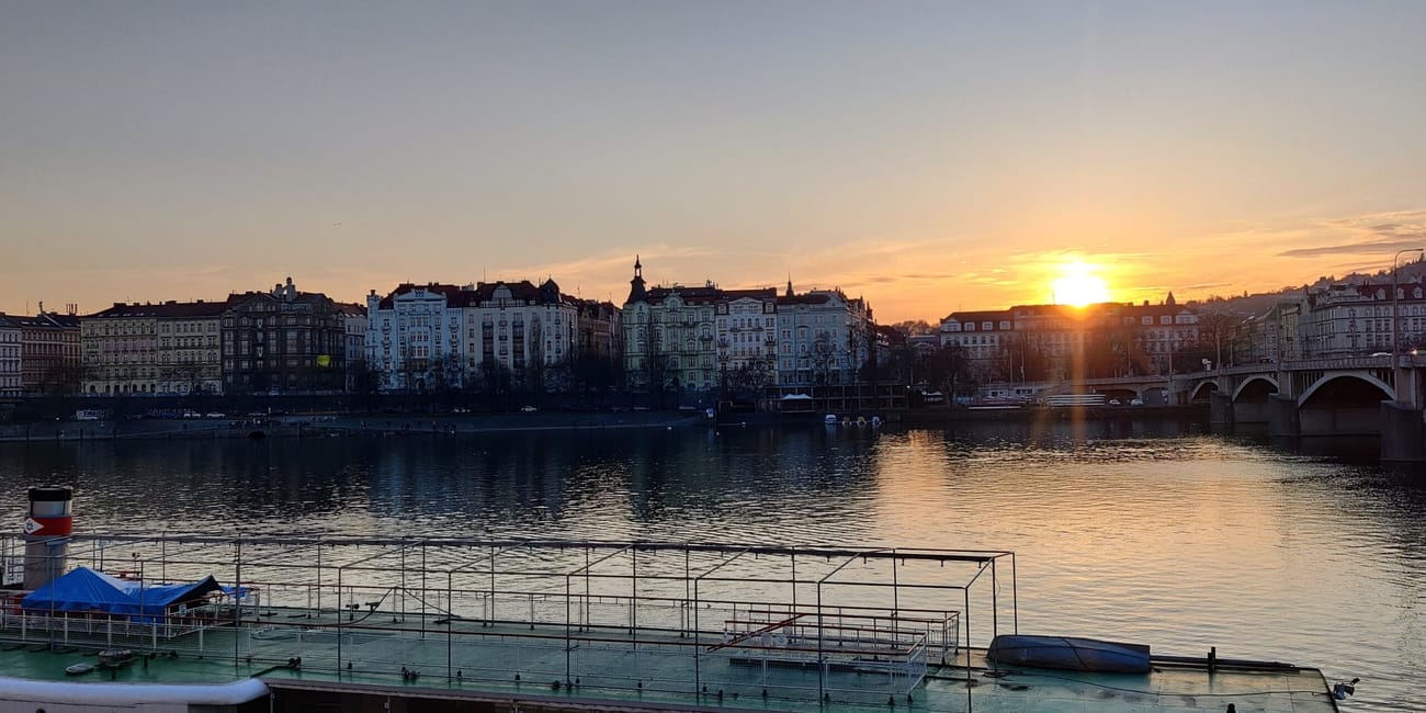 Zachód słońca nad wełtawą w pradze, z mostem i zabudową nad rzeką.