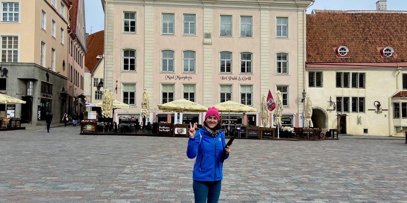 Tallinn city square in estonia with a person waving in front of historic buildings and a church spire
