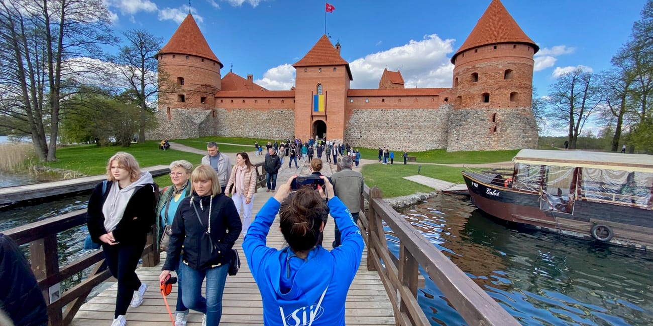 Zamek w trokach na litwie widziany z mostu, z turystami i łodzią na wodzie.
