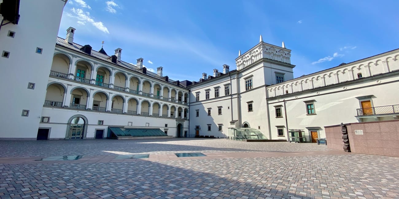 Dziedziniec zamku dolnego w wilnie z jasnymi arkadami i brukowanym placem pod błękitnym niebem