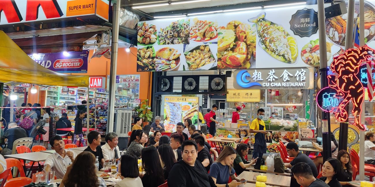 Tętniąca życiem restauracja z owocami morza w kuala lumpur, z siedzącymi gośćmi i neonowym szyldem cu cha restaurant