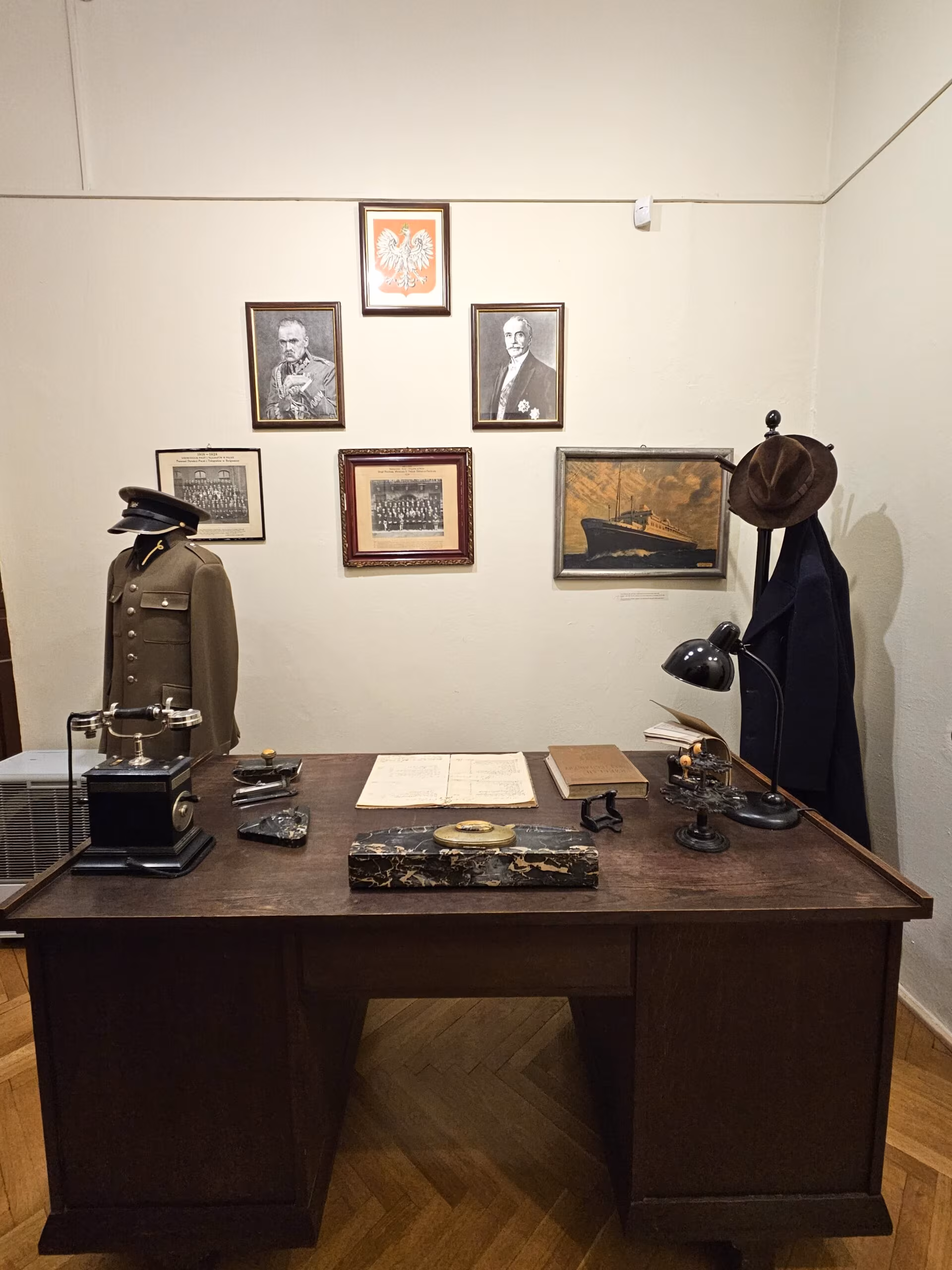 Ekspozycja w muzeum poczty polskiej w gdańsku z historycznym biurkiem, mundurem i portretami na ścianie