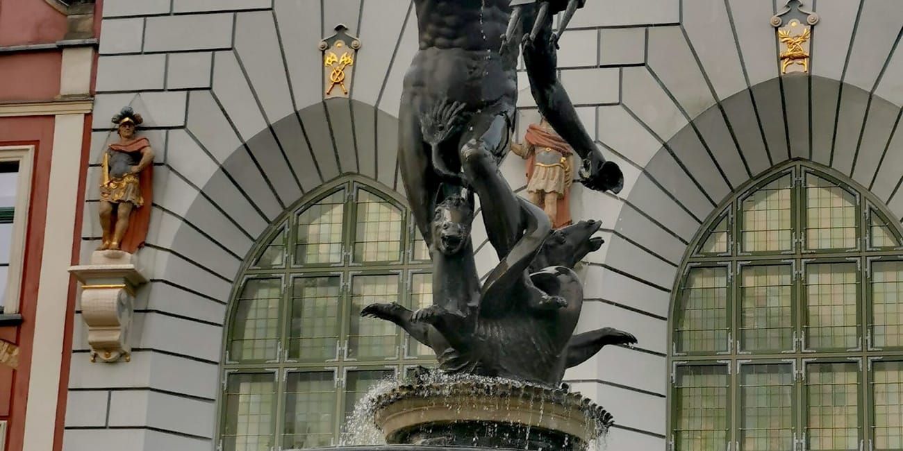 Fontanna maksymliana w gdańsku z rzeźbą neptuna przed ozdobną fasadą budynku