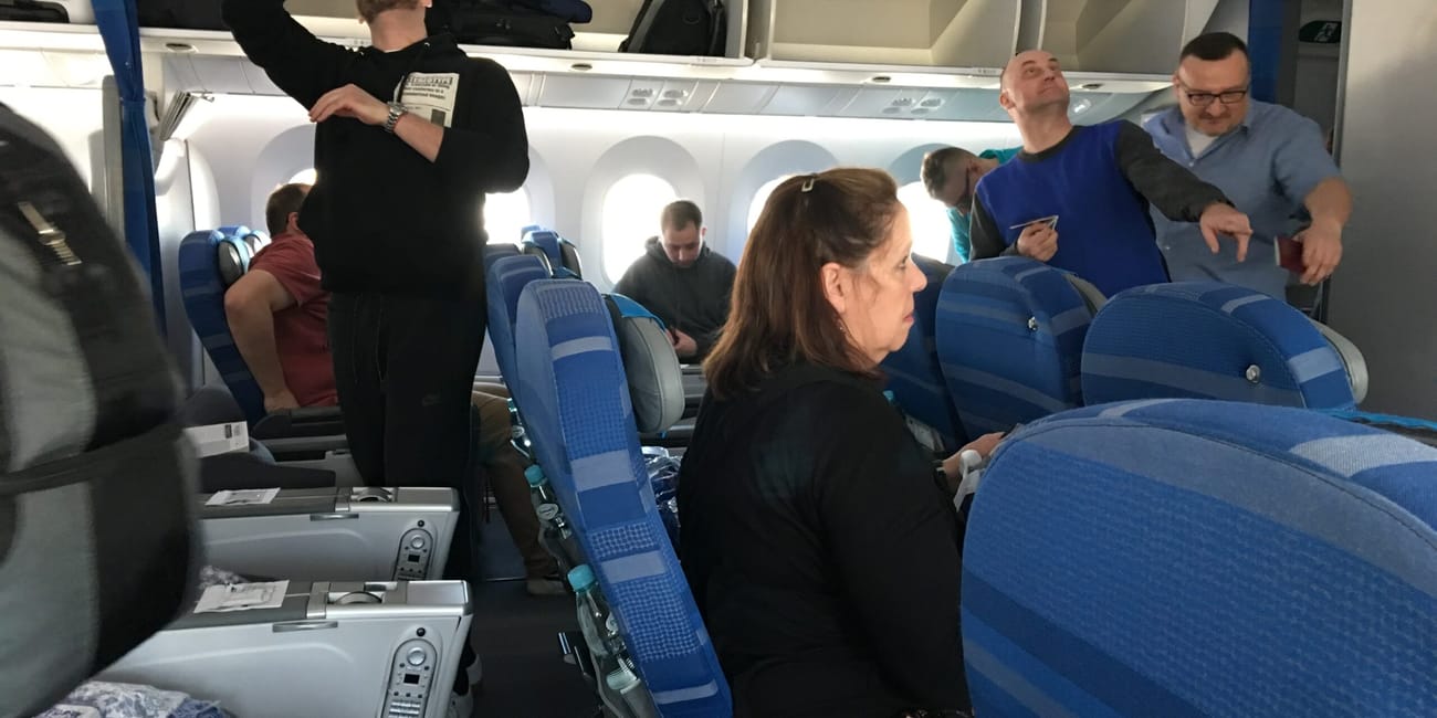Wnętrze samolotu w warszawie, pasażerowie stoją i siedzą przy miejscach.