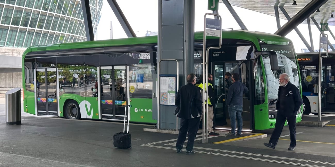 Zielony autobus na przystanku w zurychu, pasażerowie wsiadają pod nowoczesnym zadaszeniem.