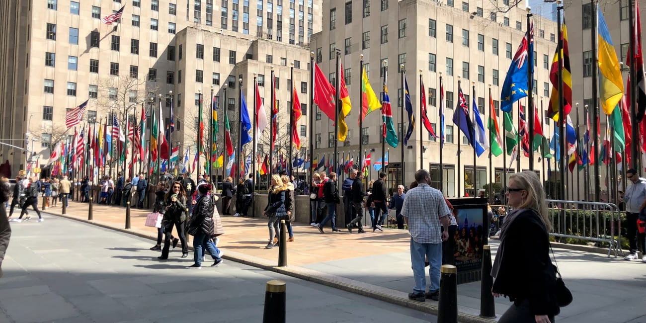 Rockefeller center w nowym jorku z rzędem kolorowych flag i przechodniami.