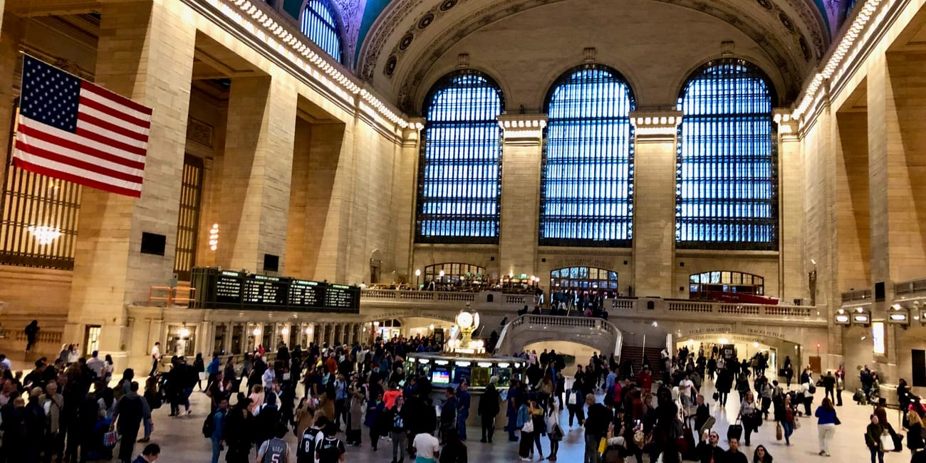 Grand central terminal w nowym jorku z dużą halą, amerykańską flagą i tłumem ludzi
