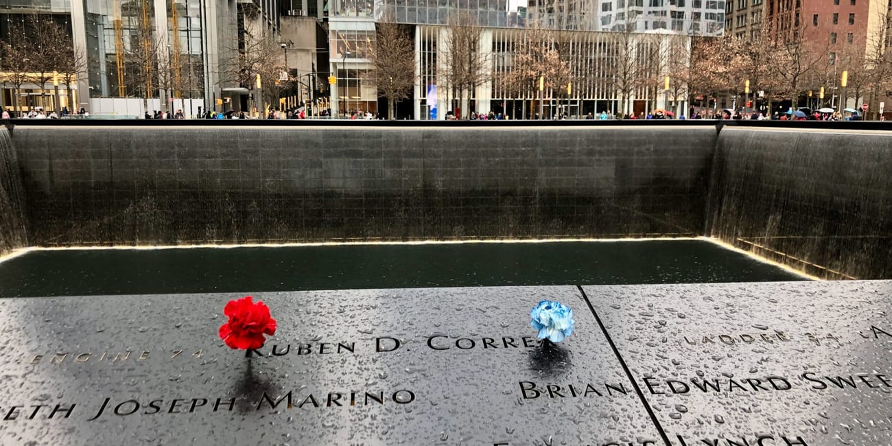 9/11 memorial pools w nowym jorku z kwiatami na czarnej płycie pamięci i kaskadą wody w tle