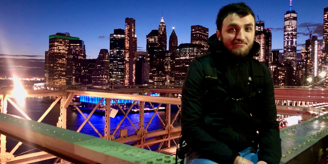 Mężczyzna siedzi na brooklyńskim moście w nowym jorku, z panoramą miasta o zmierzchu w tle