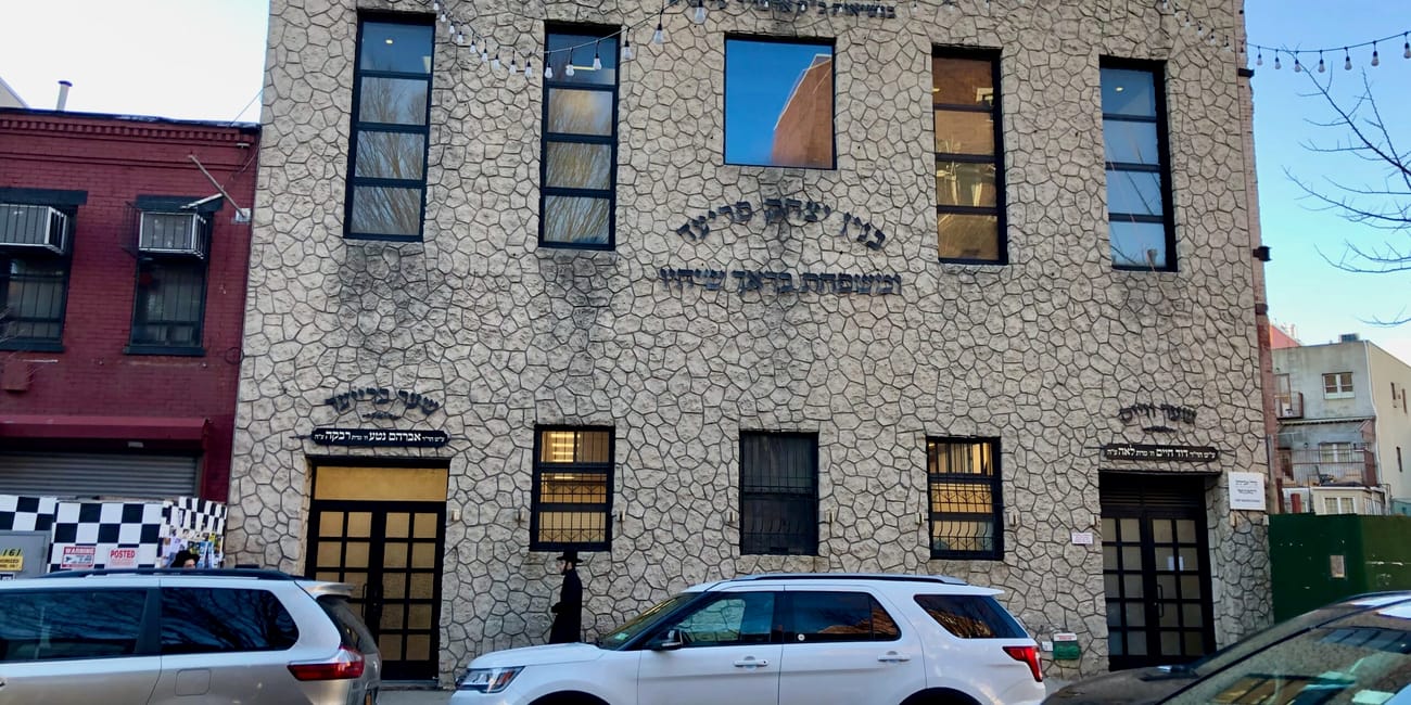 Budynek synagogi w williamsburg, nowy jork, z hebrajskimi napisami i zaparkowanymi samochodami na ulicy